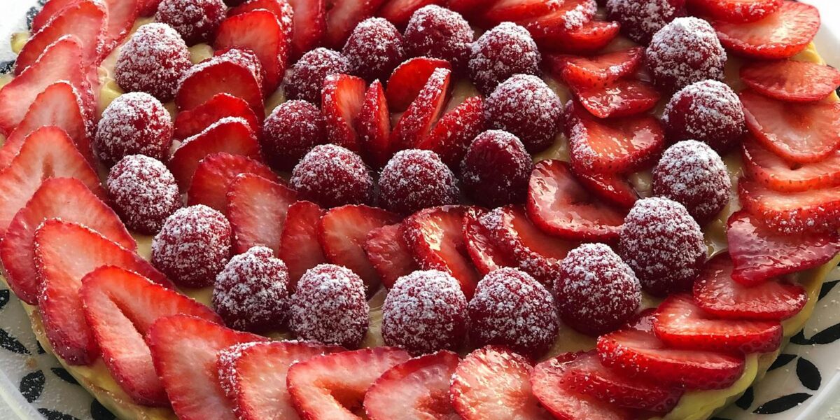 A visually stunning French tart with fresh strawberries and raspberries dusted with sugar.