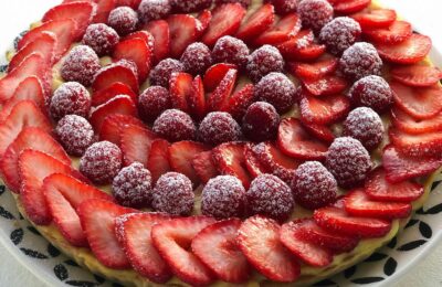 A visually stunning French tart with fresh strawberries and raspberries dusted with sugar.