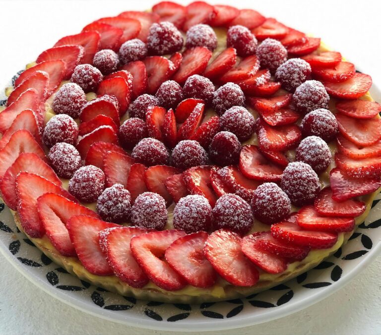 A visually stunning French tart with fresh strawberries and raspberries dusted with sugar.