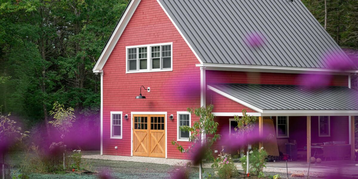 A picturesque red barn house surrounded by lush greenery and vibrant purple flowers in a peaceful rural setting.
