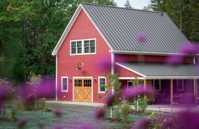A picturesque red barn house surrounded by lush greenery and vibrant purple flowers in a peaceful rural setting.