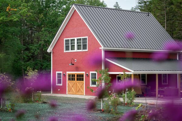 A picturesque red barn house surrounded by lush greenery and vibrant purple flowers in a peaceful rural setting.