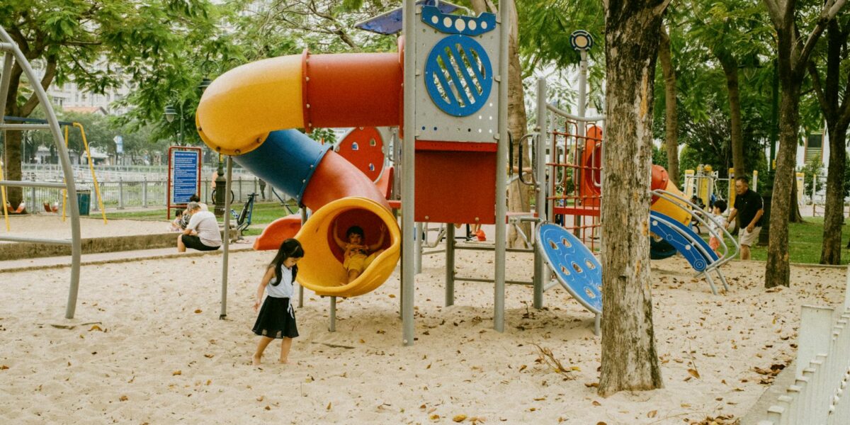 Kids enjoying colorful slides and play structures in an outdoor park playground.
