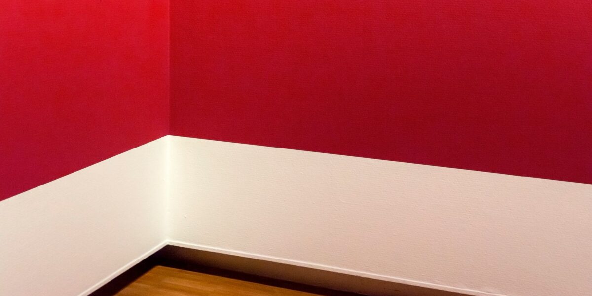 A minimalist room corner with striking red walls and wooden flooring, showcasing modern design.
