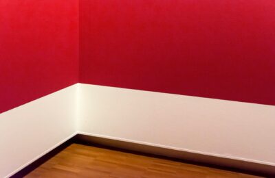 A minimalist room corner with striking red walls and wooden flooring, showcasing modern design.