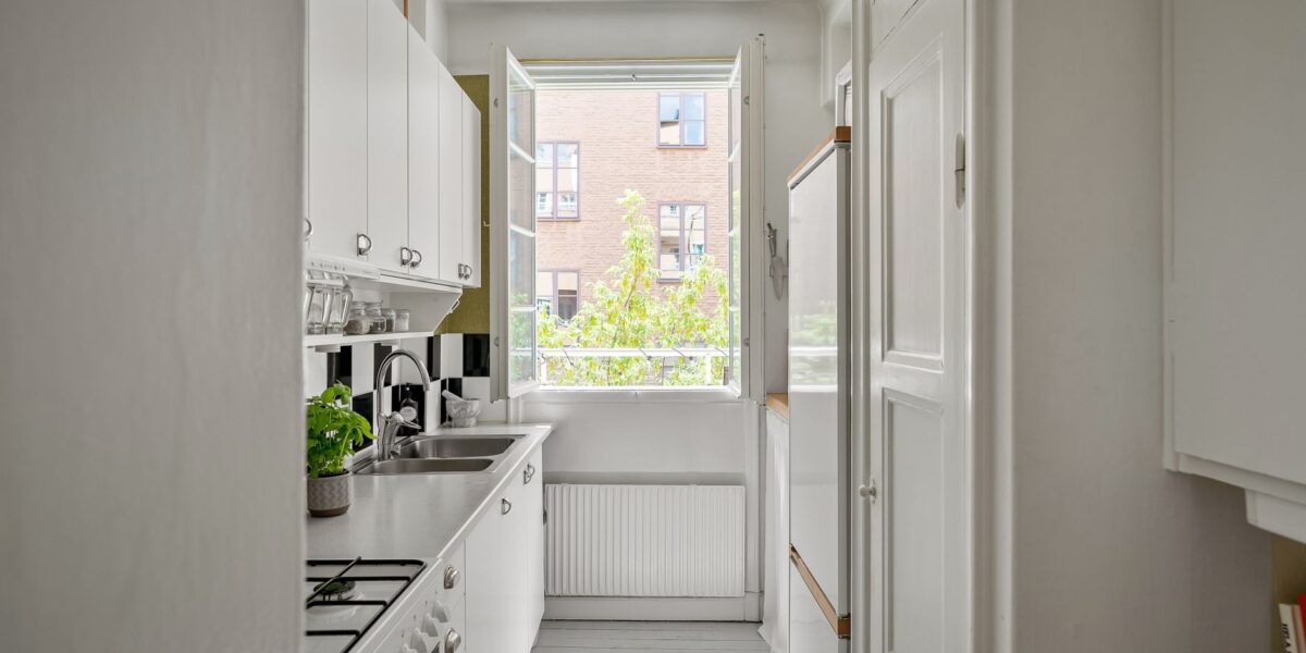 A bright and contemporary small kitchen with white cabinets and open window.