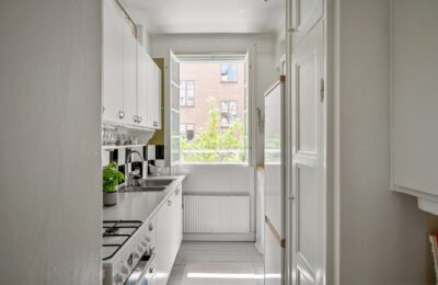 A bright and contemporary small kitchen with white cabinets and open window.