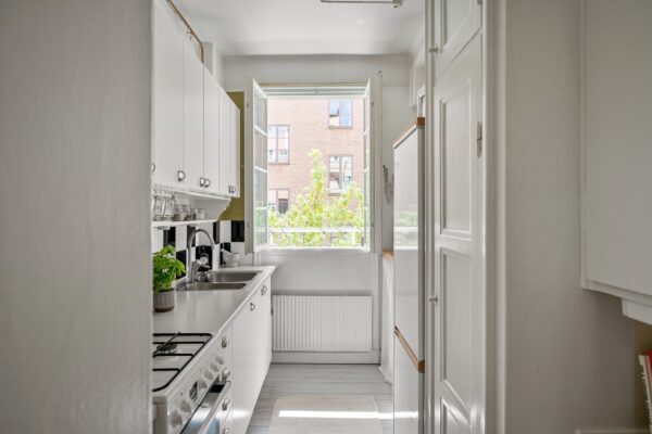A bright and contemporary small kitchen with white cabinets and open window.
