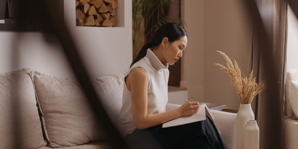 A woman sits on a sofa, taking notes in a Japandi styled living room.