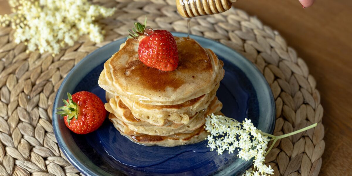 Delicious pancakes topped with fresh strawberries and honey drizzle, garnished with elderflowers.