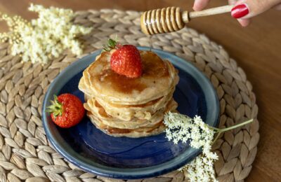 Delicious pancakes topped with fresh strawberries and honey drizzle, garnished with elderflowers.