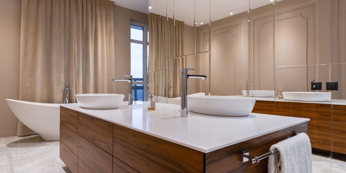 Minimalistic interior of modern bathroom with white sink and bath and mirrored cabinet in apartment in daytime