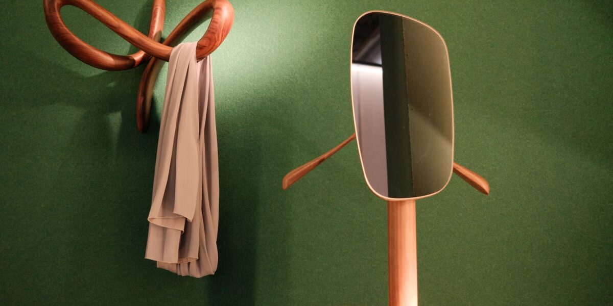 Stylish wooden hanger and mirror on green wall in Milan, creating an elegant interior design.