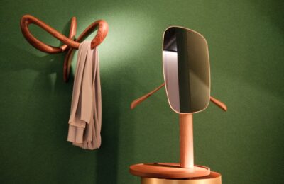 Stylish wooden hanger and mirror on green wall in Milan, creating an elegant interior design.