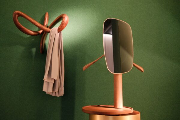 Stylish wooden hanger and mirror on green wall in Milan, creating an elegant interior design.