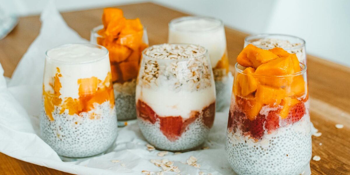 Delicious chia pudding parfaits with mango and strawberry layers on a wooden table.