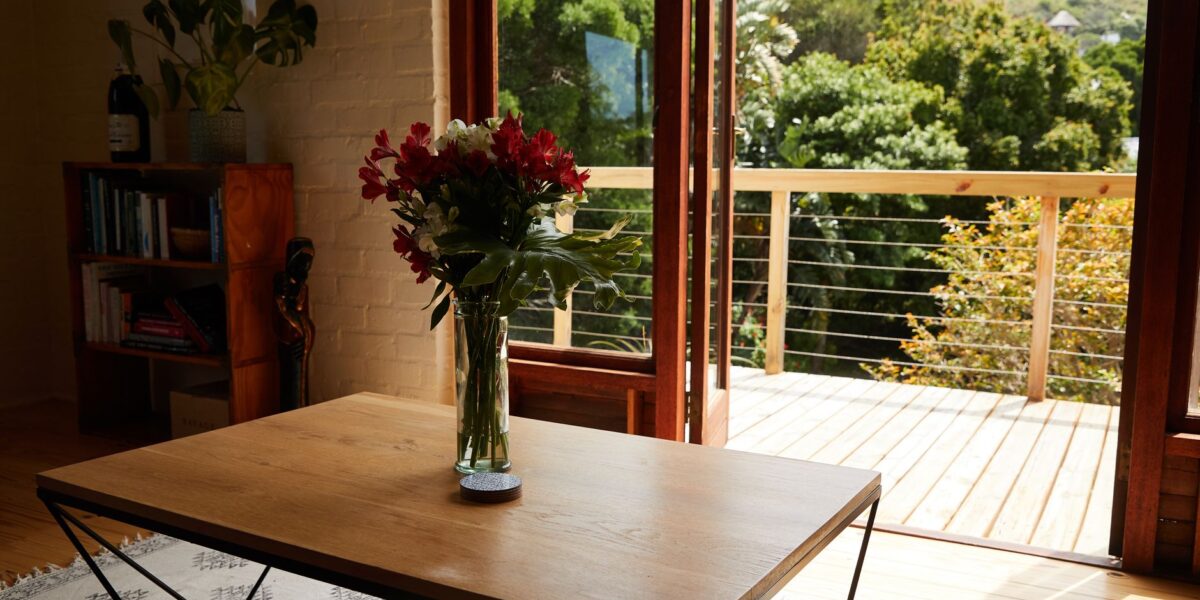 Interior of modern cozy room with timber shelf and table with delicate flowers near sunny balcony