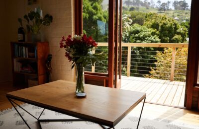 Interior of modern cozy room with timber shelf and table with delicate flowers near sunny balcony