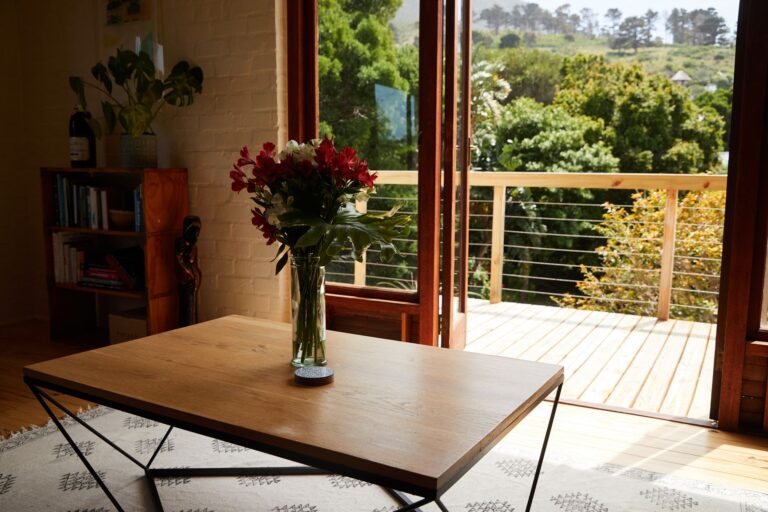 Interior of modern cozy room with timber shelf and table with delicate flowers near sunny balcony