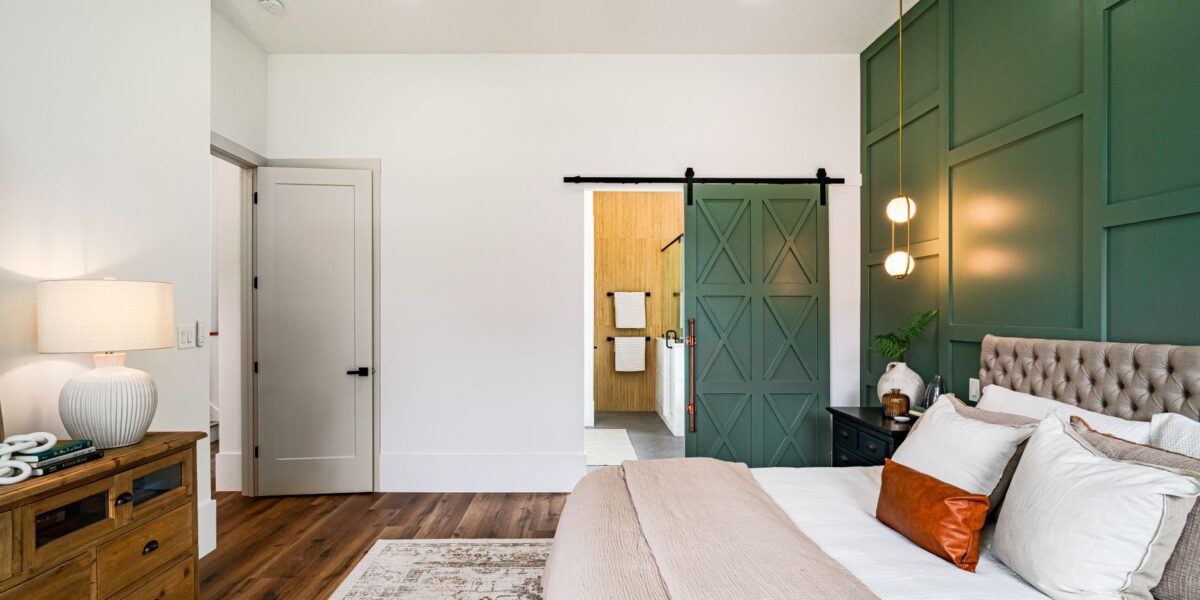 Beautiful modern bedroom with green accent wall and barn door leading to the bathroom.