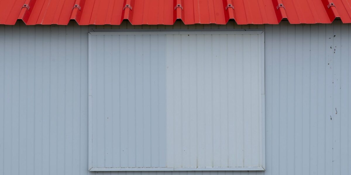 Minimalist image of a red metal roof with blue-grey corrugated panel wall.