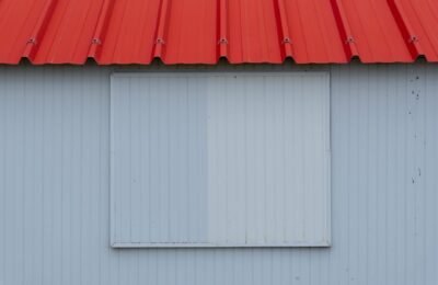Minimalist image of a red metal roof with blue-grey corrugated panel wall.