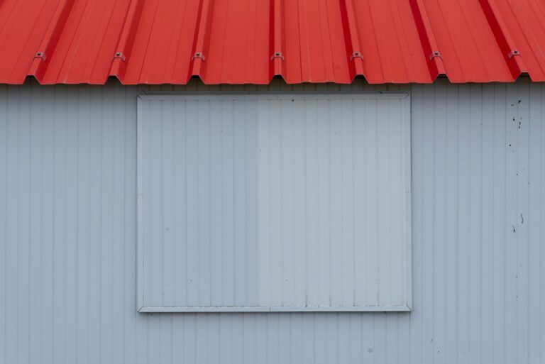 Minimalist image of a red metal roof with blue-grey corrugated panel wall.