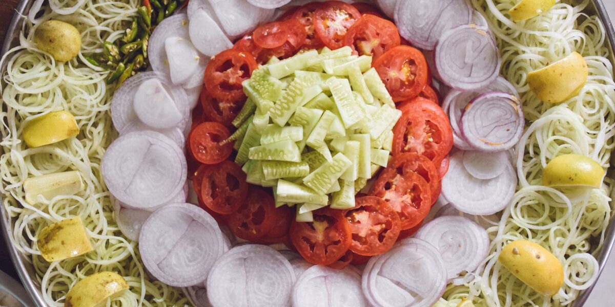 Top view of a vibrant vegetable salad platter with fresh cucumbers, tomatoes, onions, and lemons.