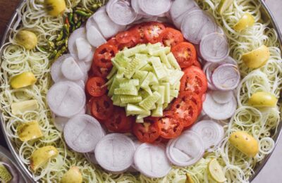 Top view of a vibrant vegetable salad platter with fresh cucumbers, tomatoes, onions, and lemons.