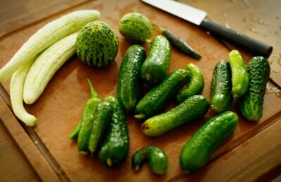 A variety of fresh cucumbers arranged on a wooden chopping board with a knife.
