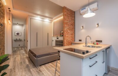 Miniature kitchen with modern appliances and bedroom behind brick partition in small loft style apartment