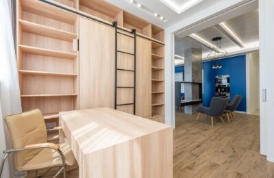 Wooden table and armchair placed near bookcase in office zone and stylish furniture in kitchen