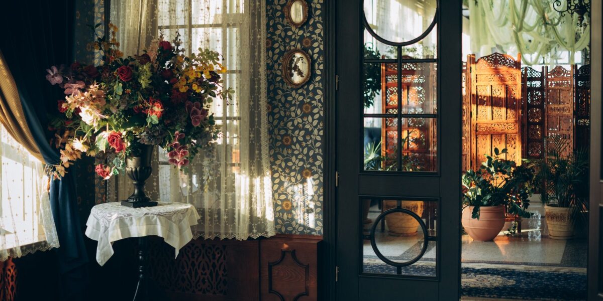 A vintage-styled room with a colorful floral bouquet and ornate door, bathed in warm sunlight.