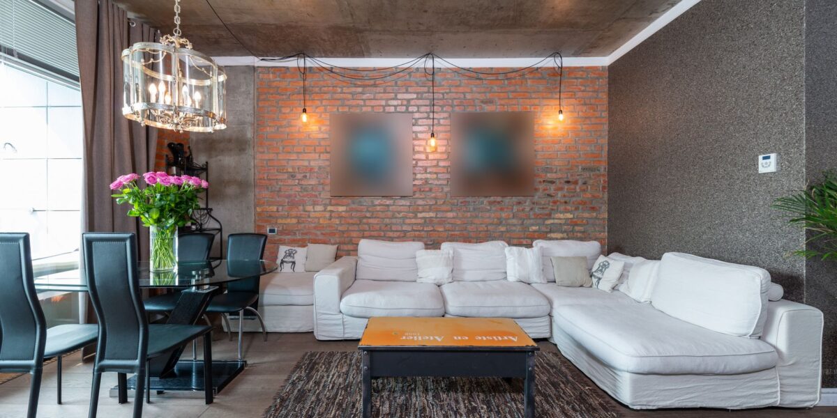 Stylish living room featuring industrial design with brick wall, white sofa, and chic chandelier.