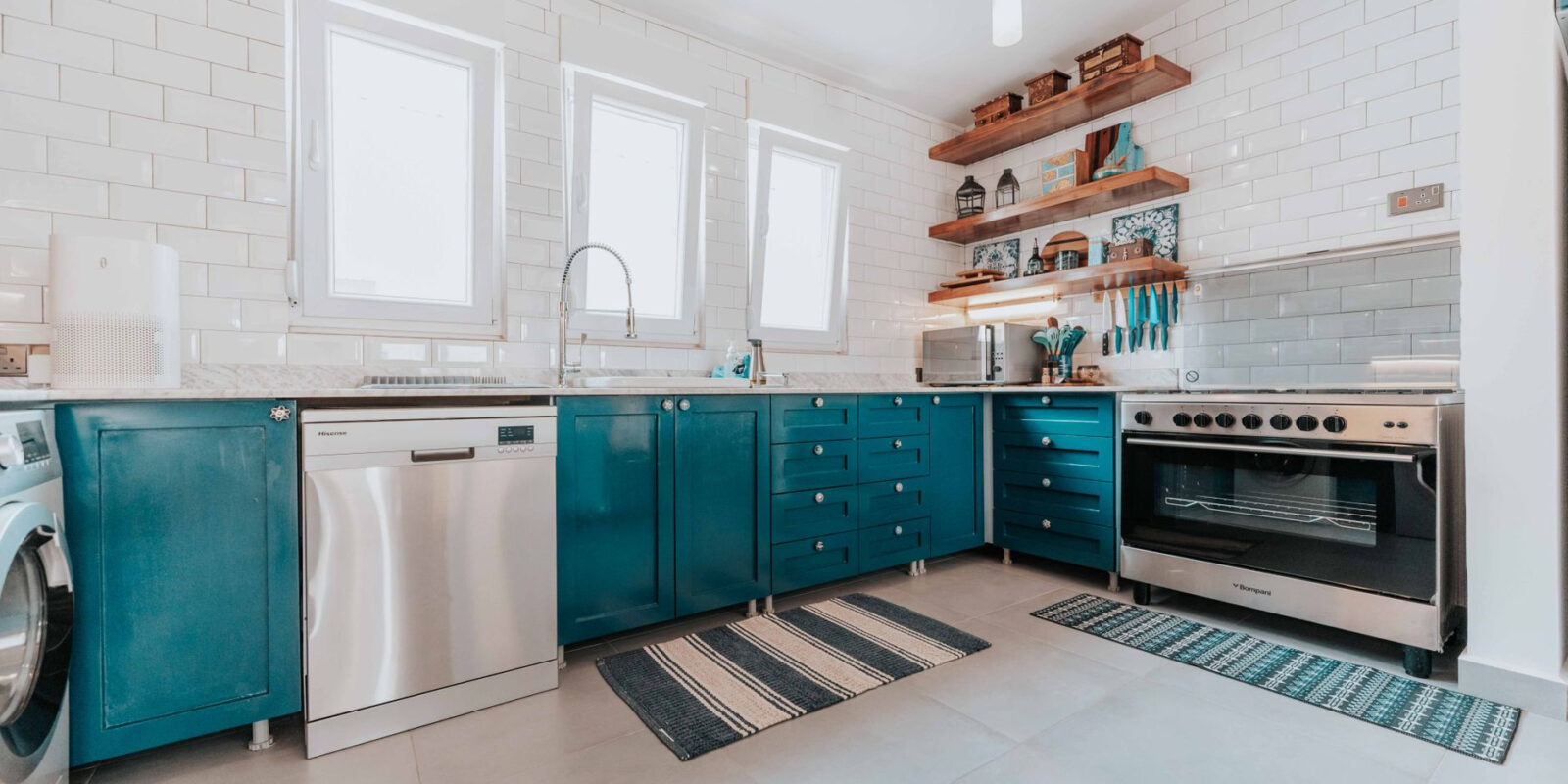 Bright modern kitchen with blue cabinets, stainless steel appliances, and open shelving.