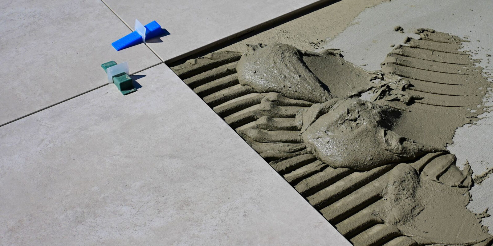 Close-up of wet cement and tile spacers during floor tile installation.