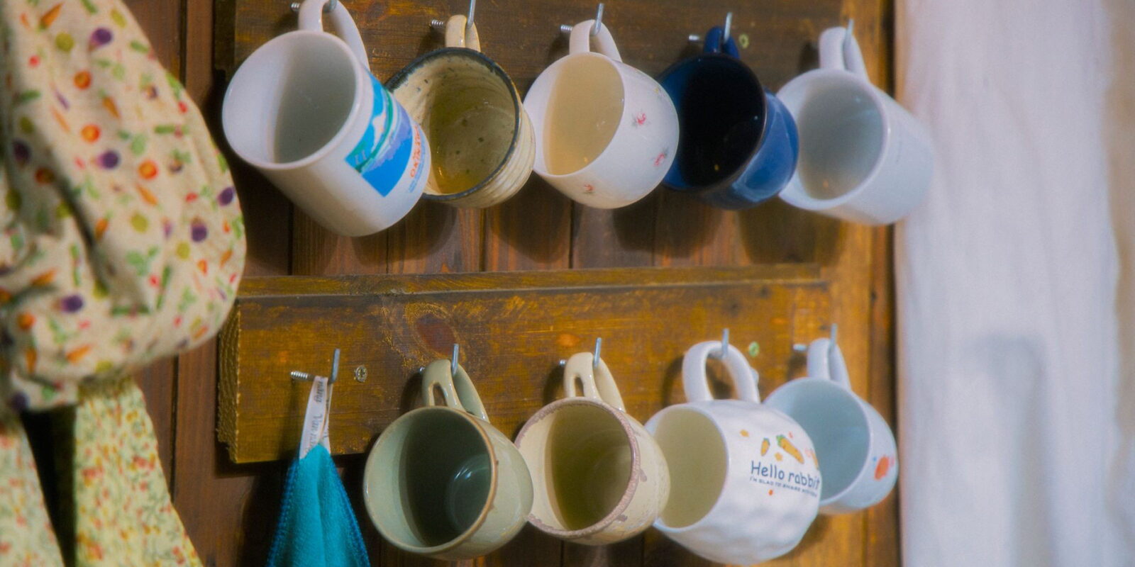 Rustic wooden rack with ceramic mugs hanging neatly, evoking cozy kitchen vibes.