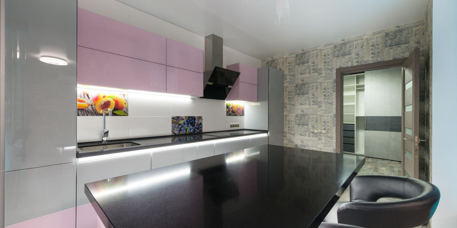Black table with chairs placed near colorful cupboards and modern kitchenware in stylish kitchen with opened door in spacious apartment
