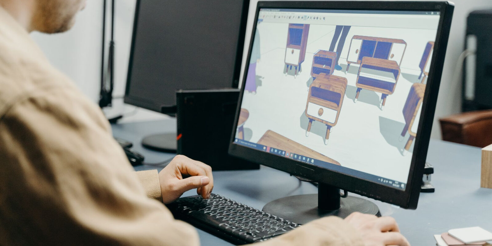 A product designer using a computer for 3D furniture modeling in an office setting.
