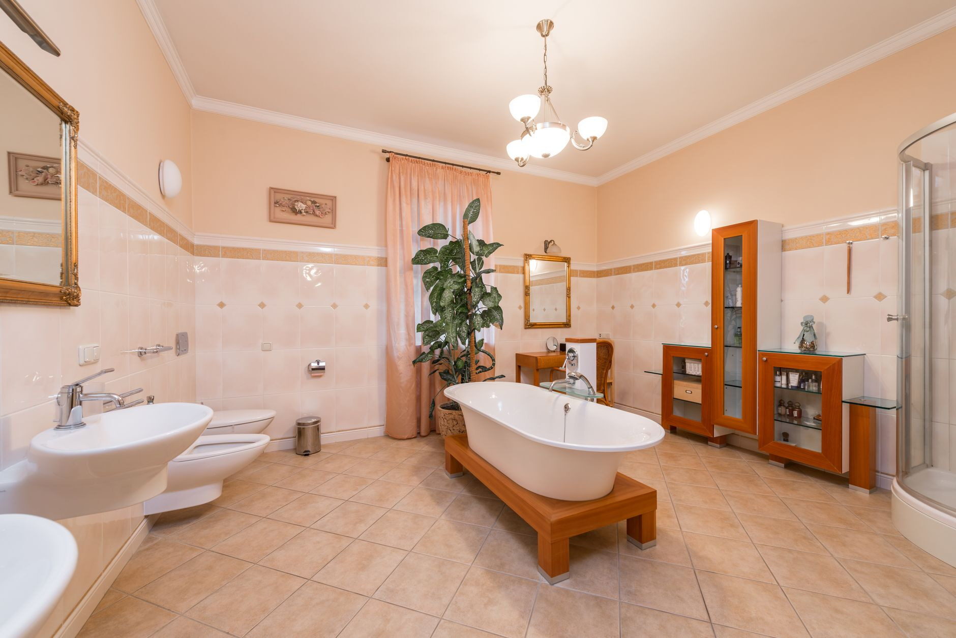 Interior design of bathroom with bathtub in centre and shower cabin next to cabinet and table with mirror opposite toilet and bidet near sink and mirror