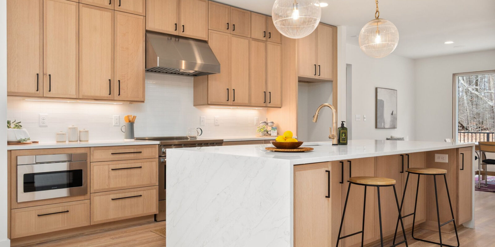 Bright modern kitchen with wood cabinets, marble island, and pendant lights, epitomizing Scandinavian design.