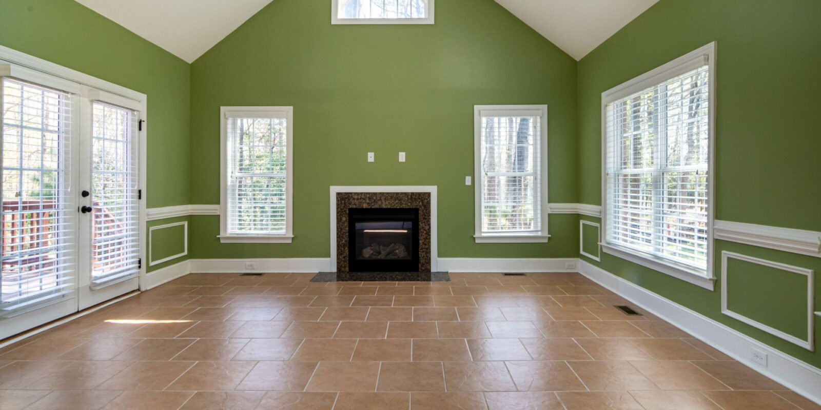 Elegant empty living room featuring green walls, a fireplace, and tiled flooring.