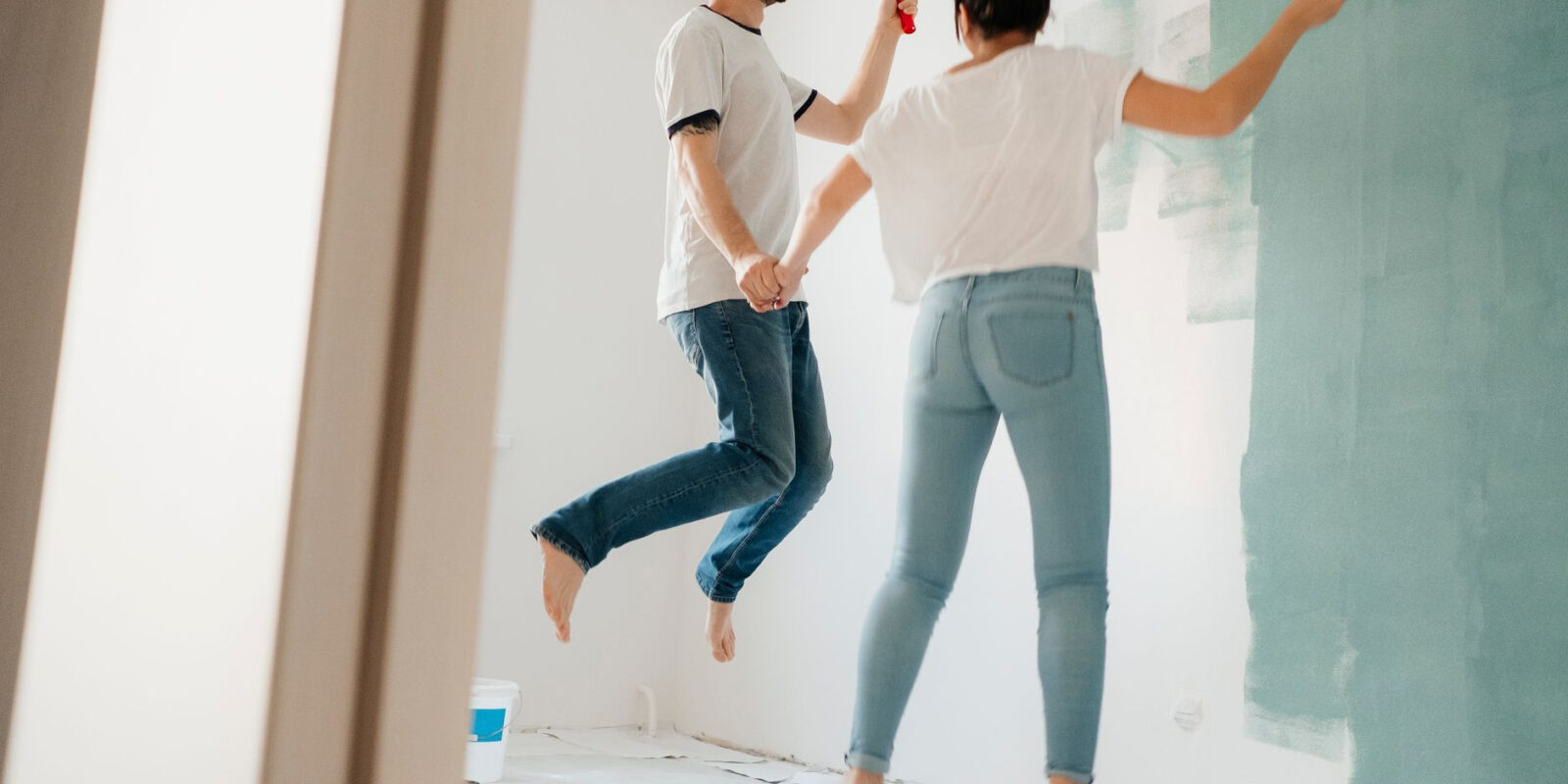 A playful couple painting walls together in their home, having fun while holding hands.